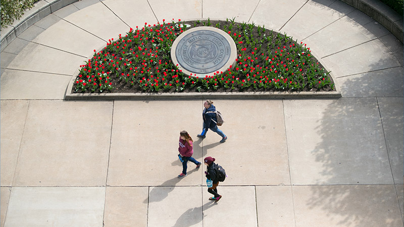 Indoor photo of students walking by some flowers
